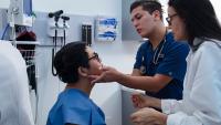 Nursing student practicing clinical skills on a patient with an instructor overseeing.